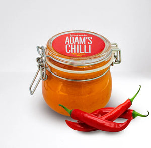 Glass jar of homemade Adam's Chilli with red chili peppers, plant-based spicy sauce
