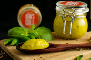 Vegan green chilli paste in glass jar and wooden spoon, fresh herbs on cutting board