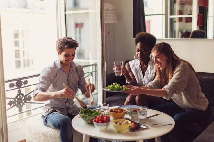 Three friends sharing plant-based vegan food at home, enjoying healthy meals around a table.