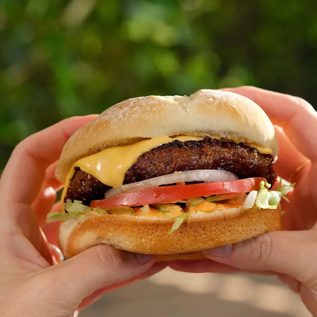 Hand holding a plant-based burger with vegan cheese, tomato, lettuce, and onion